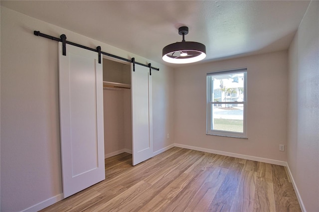 1933 Oregon Trl, Englewood, FL 34224 - unfurnished bedroom featuring a barn door, light wood-type flooring, baseboards, and a closet