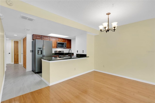 2020 Royal Bay Blvd Unit 91, Kissimmee, FL 34746 - kitchen with stainless steel appliances, a chandelier, dark countertops, a peninsula, and light wood-style floors