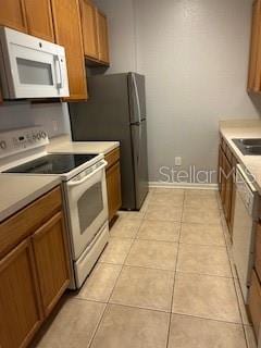 8775 Sartori St Unit 307, Orlando, FL 32829 - kitchen featuring white appliances, brown cabinets, light countertops, a sink, and baseboards