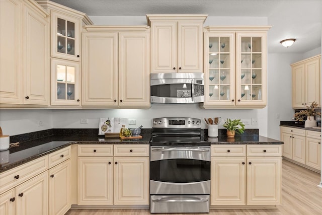 3868 Whitewood Ct, Oviedo, FL 32766 - kitchen featuring appliances with stainless steel finishes, cream cabinets, dark stone counters, and glass insert cabinets