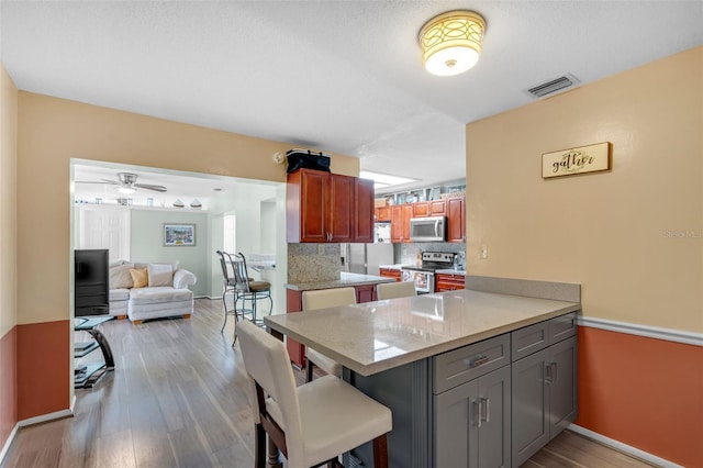 7500 NW 66th Ter, Tamarac, FL 33321 - kitchen featuring stainless steel appliances, a peninsula, light wood-style flooring, backsplash, and baseboards