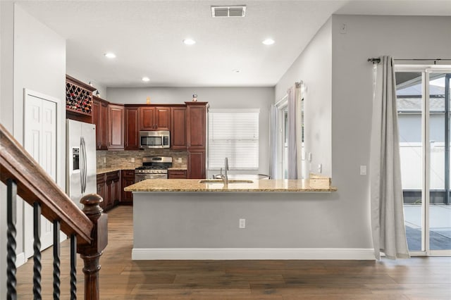5032 Beach River Rd, Windermere, FL 34786 - kitchen featuring appliances with stainless steel finishes, a sink, light stone counters, wood finished floors, and backsplash