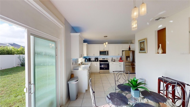 3044 Camino Real Dr S, Kissimmee, FL 34744 - kitchen featuring appliances with stainless steel finishes, light countertops, light tile patterned floors, white cabinetry, and hanging light fixtures