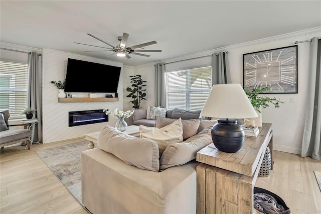 living room featuring ceiling fan, ornamental molding, healthy amount of natural light, a glass covered fireplace, and wood finished floors