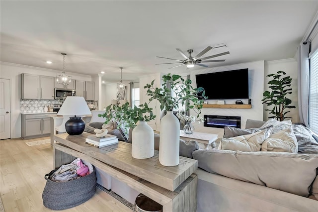 living room featuring a glass covered fireplace, a ceiling fan, crown molding, light wood-type flooring, and plenty of natural light