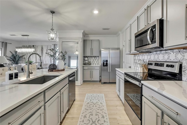 kitchen with stainless steel appliances, a sink, a chandelier, backsplash, and light wood-style floors