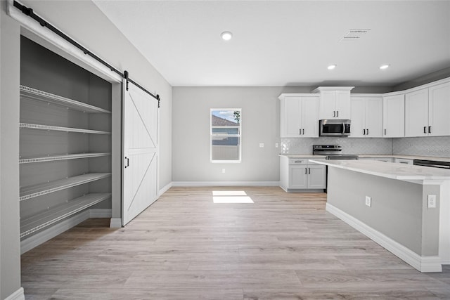 3944 SW 130th Loop, Ocala, FL 34473 - kitchen with appliances with stainless steel finishes, a barn door, white cabinets, backsplash, and baseboards