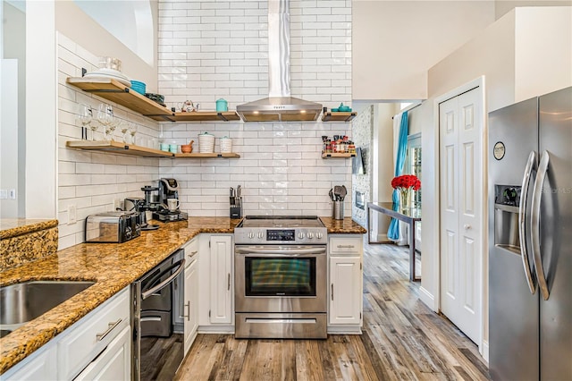 7838 Rollingridge Ct, Orlando, FL 32835 - kitchen featuring appliances with stainless steel finishes, wall chimney exhaust hood, backsplash, white cabinetry, and light wood-type flooring