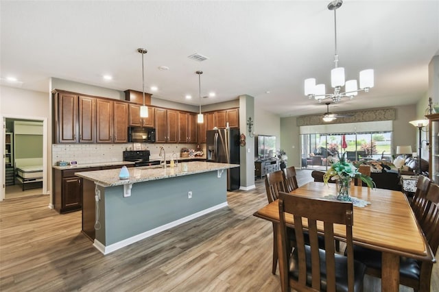 2941 Marlberry Ln, Clermont, FL 34714 - kitchen with black appliances, a chandelier, backsplash, an island with sink, and light wood-style floors