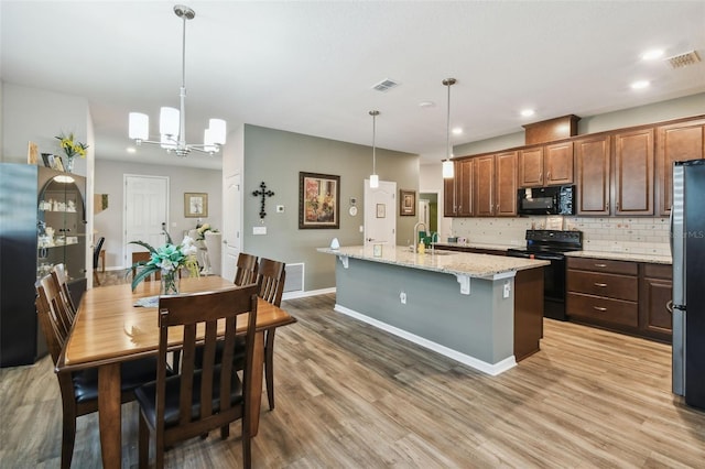 2941 Marlberry Ln, Clermont, FL 34714 - kitchen with black appliances, decorative backsplash, an island with sink, light wood-type flooring, and a breakfast bar