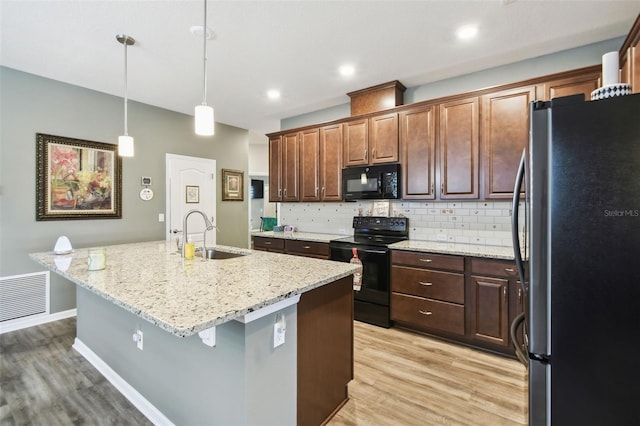 2941 Marlberry Ln, Clermont, FL 34714 - kitchen featuring black appliances, light wood-style flooring, a center island with sink, tasteful backsplash, and recessed lighting