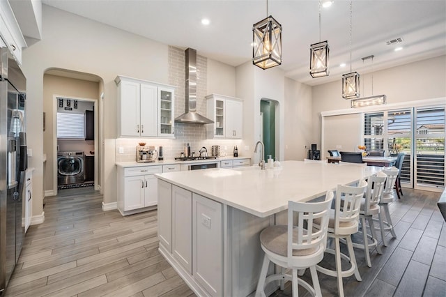 29043 Picana Ln, Wesley Chapel, FL 33543 - kitchen featuring wall chimney range hood, washer / dryer, arched walkways, light wood finished floors, and recessed lighting