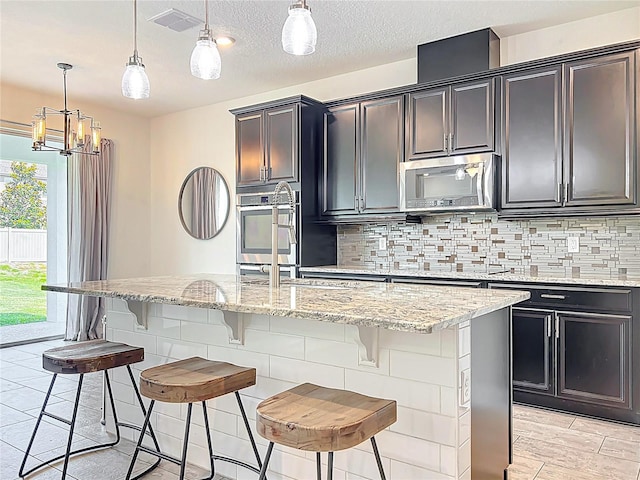 3184 Pinenut Dr, Apopka, FL 32712 - kitchen featuring stainless steel microwave, light stone countertops, pendant lighting, a chandelier, and a breakfast bar