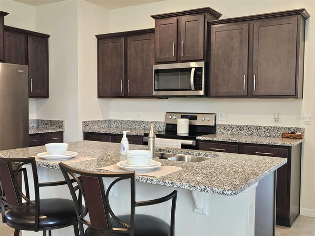 3371 Yellowtop Loop, Clermont, FL 34714 - kitchen featuring stainless steel appliances, dark brown cabinets, a center island with sink, a kitchen breakfast bar, and light stone counters