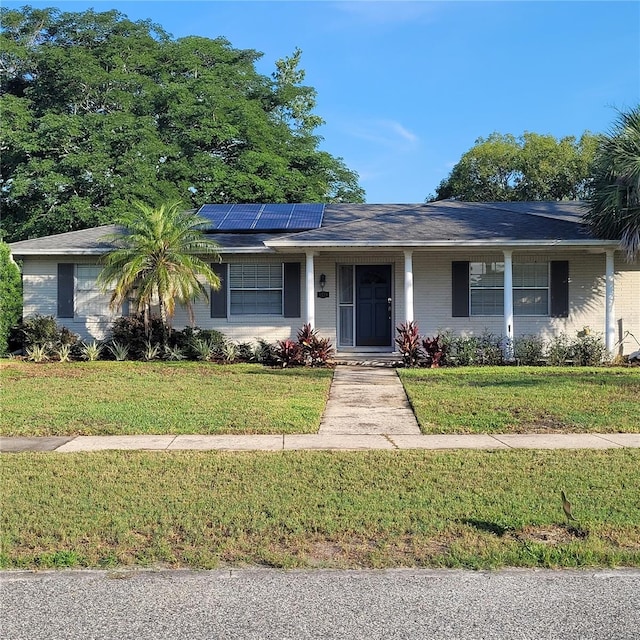 8539 Clematis Ln, Orlando, FL 32819 - ranch-style house featuring solar panels, a front yard, covered porch, and brick siding