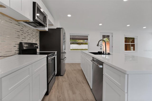 4201 Mizell St, Orlando, FL 32812 - kitchen featuring stainless steel appliances, a sink, light wood-style flooring, white cabinets, and backsplash