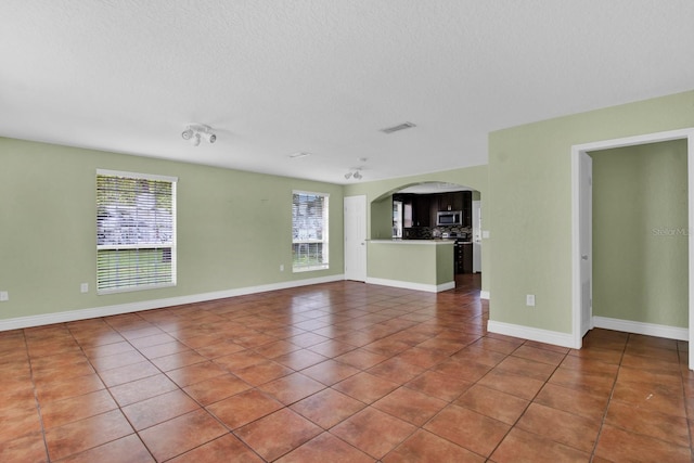 416 Banyon Tree Cir Unit 108, Maitland, FL 32751 - unfurnished living room featuring healthy amount of natural light, tile patterned flooring, arched walkways, baseboards, and a textured ceiling