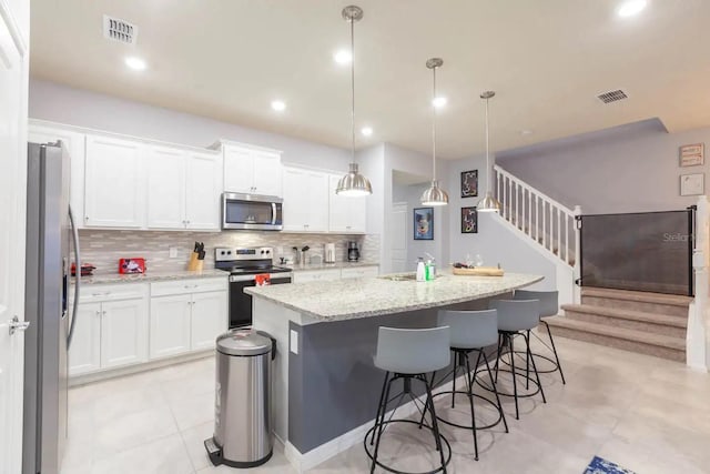 271 Jetty Way, Davenport, FL 33897 - kitchen featuring appliances with stainless steel finishes, decorative backsplash, a kitchen island with sink, white cabinets, and a breakfast bar