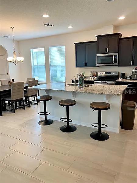 16391 Admirals Cove Ln, Winter Garden, FL 34787 - kitchen featuring stainless steel appliances, a breakfast bar area, light stone counters, a chandelier, and a center island with sink
