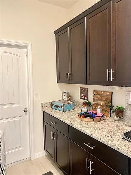 16391 Admirals Cove Ln, Winter Garden, FL 34787 - kitchen featuring light tile patterned floors, light stone counters, and dark brown cabinetry