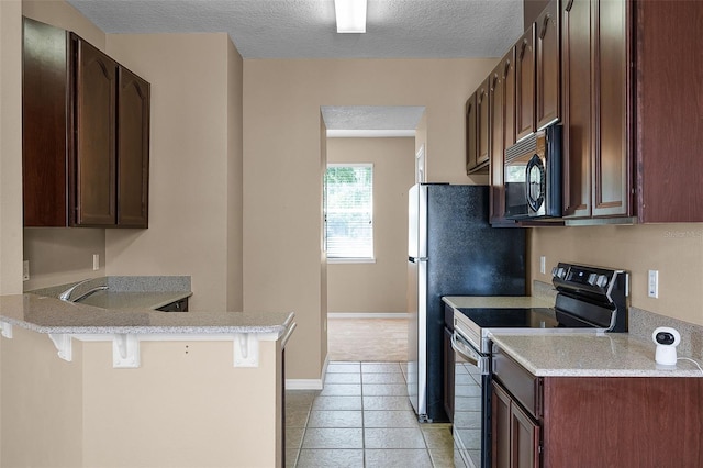 12335 Cruxbury Dr, Windermere, FL 34786 - kitchen featuring black appliances, a breakfast bar area, a peninsula, a textured ceiling, and light countertops