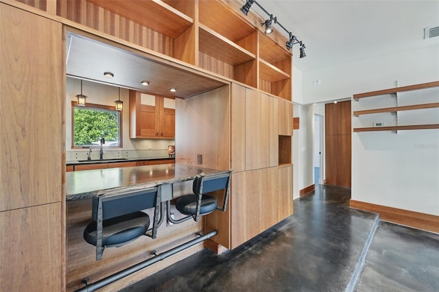 6327 Ridgeberry Dr, Orlando, FL 32819 - kitchen featuring concrete floors, brown cabinetry, open shelves, dark stone countertops, and a kitchen bar