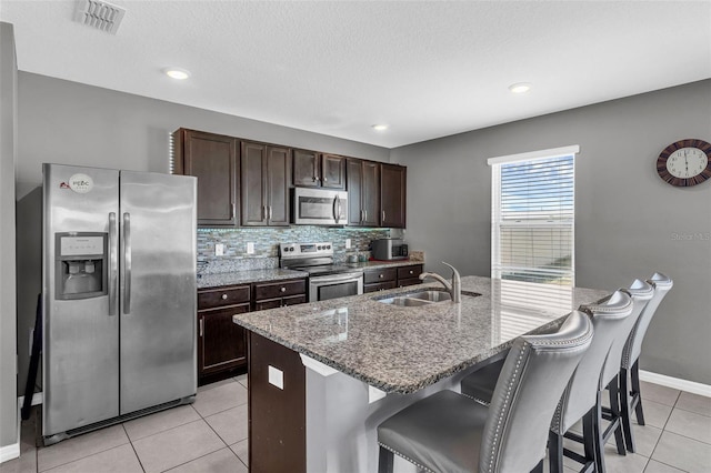 269 Ludisia Loop, Davenport, FL 33837 - kitchen featuring stainless steel appliances, a sink, light tile patterned floors, dark brown cabinets, and a kitchen bar