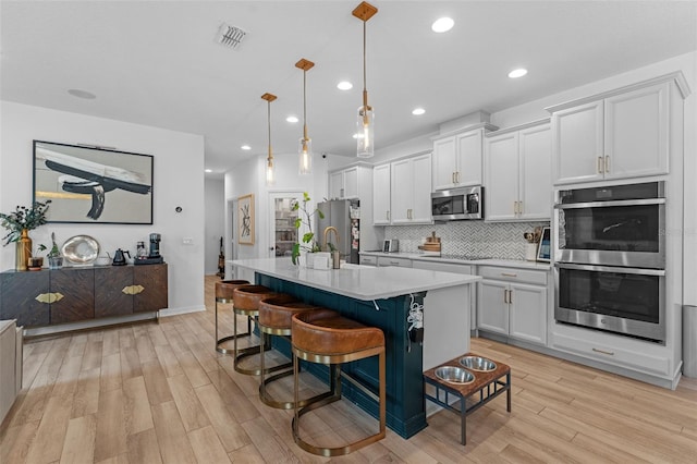 1425 Paget Cv, Sanford, FL 32771 - kitchen featuring appliances with stainless steel finishes, light wood finished floors, light countertops, a center island with sink, and backsplash