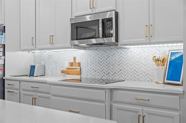 1425 Paget Cv, Sanford, FL 32771 - kitchen featuring stainless steel microwave, light countertops, black electric cooktop, backsplash, and white cabinets