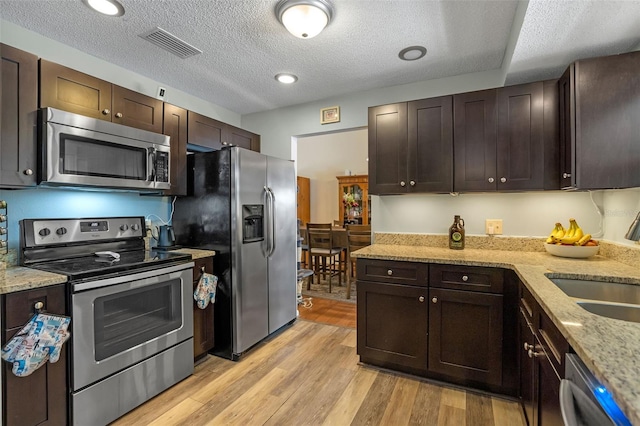 3362 Partridge St, Deltona, FL 32738 - kitchen featuring appliances with stainless steel finishes, a sink, light wood-type flooring, dark brown cabinets, and light stone countertops