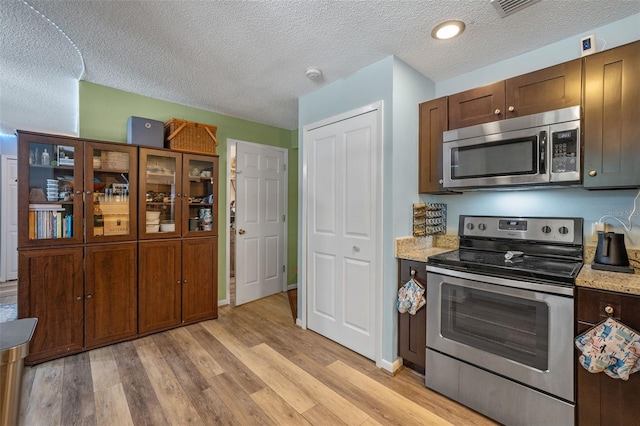 3362 Partridge St, Deltona, FL 32738 - kitchen featuring appliances with stainless steel finishes, light wood-type flooring, a textured ceiling, light stone countertops, and glass insert cabinets