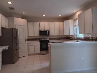 10415 Lucaya Dr, Tampa, FL 33647 - kitchen featuring stainless steel appliances, a peninsula, recessed lighting, light tile patterned flooring, and white cabinets