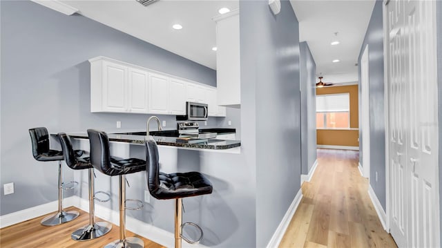 5016 W Lancaster St Unit 00, Tampa, FL 33616 - kitchen with stainless steel appliances, light wood finished floors, a breakfast bar, white cabinets, and recessed lighting