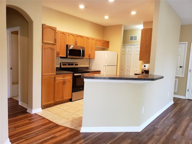 3658 Oakdale Cir Unit 100, Oviedo, FL 32765 - kitchen featuring appliances with stainless steel finishes, wood finished floors, dark countertops, arched walkways, and a peninsula