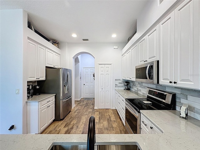 27143 Nostalgia Dr, Leesburg, FL 34748 - kitchen featuring appliances with stainless steel finishes, a sink, arched walkways, white cabinets, and recessed lighting