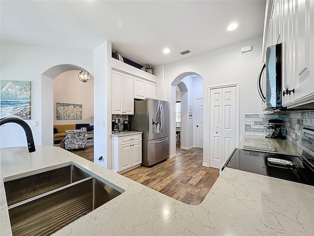 27143 Nostalgia Dr, Leesburg, FL 34748 - kitchen featuring appliances with stainless steel finishes, a sink, arched walkways, light stone countertops, and white cabinets