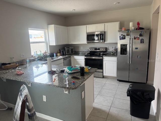268 Fiddlewood Ct, Davenport, FL 33837 - kitchen with stainless steel appliances, a peninsula, white cabinetry, dark stone counters, and a sink