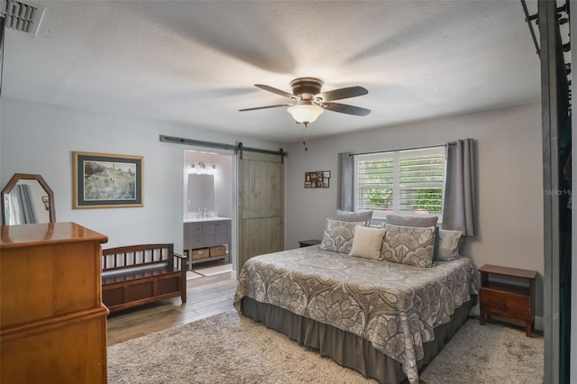 704 Tangerine Ct, Winter Garden, FL 34787 - bedroom with a barn door, a textured ceiling, wood finished floors, connected bathroom, and ceiling fan