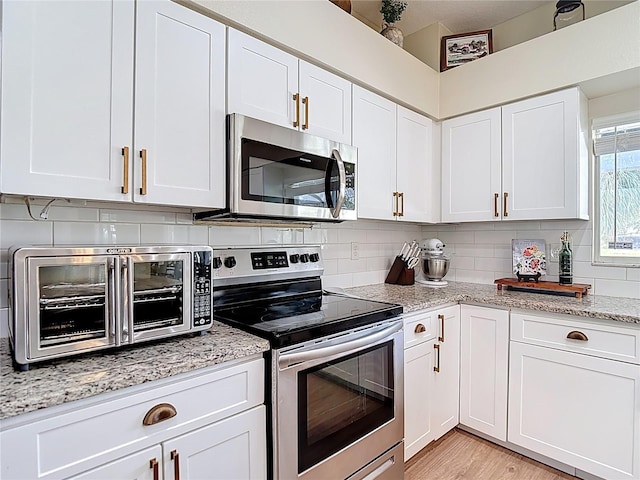 18109 Kara Ct, Tampa, FL 33647 - kitchen featuring appliances with stainless steel finishes, tasteful backsplash, white cabinetry, light stone counters, and light wood finished floors