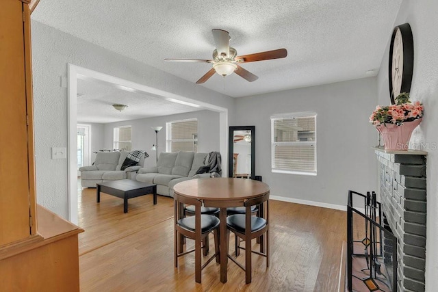 232 E Grant St, Orlando, FL 32806 - dining space with a ceiling fan, a textured ceiling, light wood-style flooring, a fireplace, and baseboards