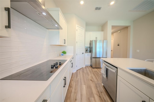 16055 Silver Brook Way, Winter Garden, FL 34787 - kitchen featuring appliances with stainless steel finishes, wall chimney range hood, light wood finished floors, white cabinetry, and tasteful backsplash