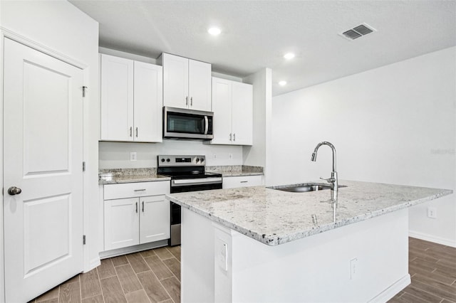 1740 Brekey Way, Zephyrhills, FL 33541 - kitchen with appliances with stainless steel finishes, wood finish floors, a kitchen island with sink, light stone counters, and white cabinetry