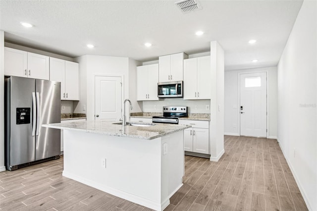1740 Brekey Way, Zephyrhills, FL 33541 - kitchen featuring stainless steel appliances, light wood-type flooring, an island with sink, white cabinets, and recessed lighting