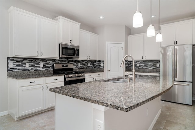 7308 Hermes Ct, Apollo Beach, FL 33572 - kitchen featuring appliances with stainless steel finishes, a sink, tasteful backsplash, dark stone countertops, and a center island with sink