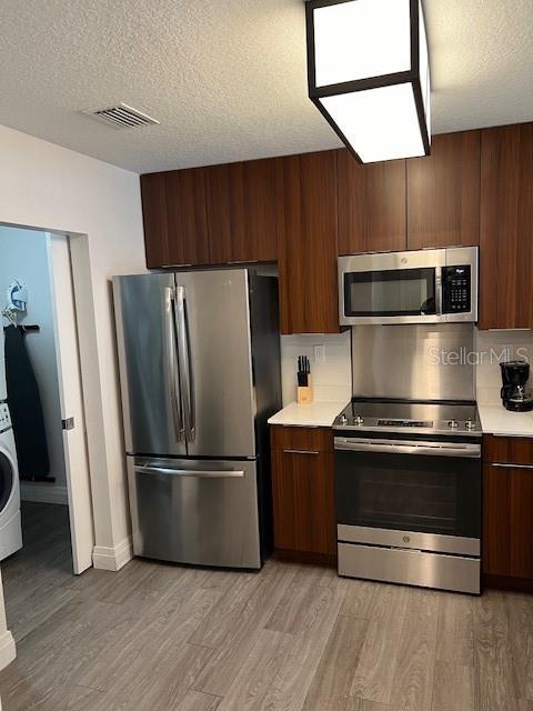 14501 Grove Resort Ave Unit 2129, Winter Garden, FL 34787 - kitchen featuring appliances with stainless steel finishes, light countertops, modern cabinets, light wood-style flooring, and a textured ceiling