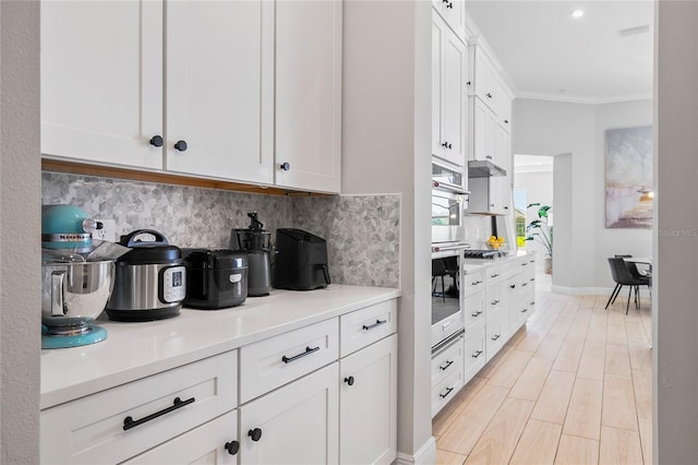 4754 Manning Ct, Sarasota, FL 34240 - kitchen with ornamental molding, white cabinetry, under cabinet range hood, light countertops, and backsplash