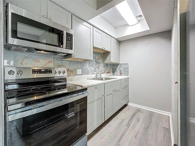 6100 12th St S Unit 313, Saint Petersburg, FL 33705 - kitchen featuring appliances with stainless steel finishes, light wood-style floors, a sink, tasteful backsplash, and baseboards