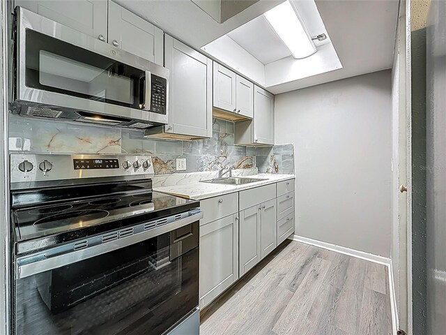 6100 12th St S Unit 313, Saint Petersburg, FL 33705 - kitchen featuring appliances with stainless steel finishes, light wood-style floors, a sink, decorative backsplash, and baseboards