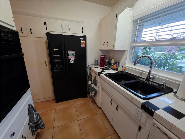 663 68th Ave S, Saint Petersburg, FL 33705 - kitchen featuring black appliances, tile countertops, a sink, white cabinets, and light tile patterned flooring
