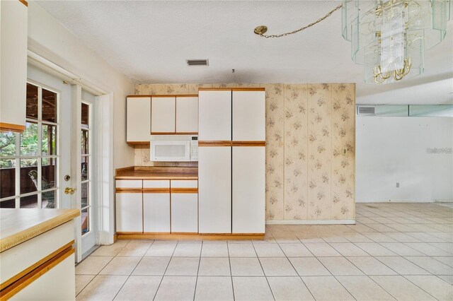 7024 Harwick Dr, Orlando, FL 32818 - kitchen with white microwave, baseboards, a chandelier, light tile patterned flooring, and white cabinetry